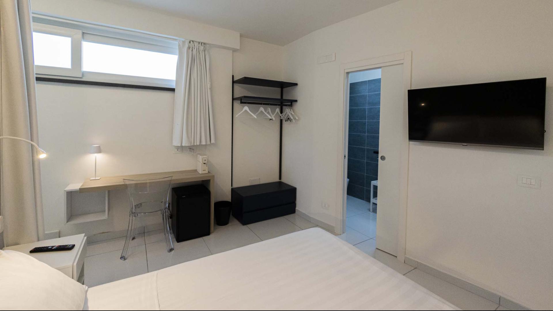 Camera moderna, luminosa, minimalista con bagno elegante e TV a parete.