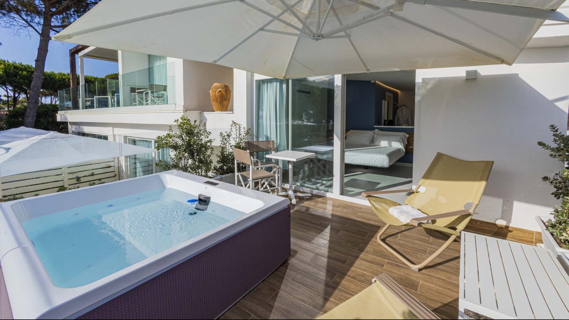 Terrazza rilassante con jacuzzi, lettini e vista su giardino verde.