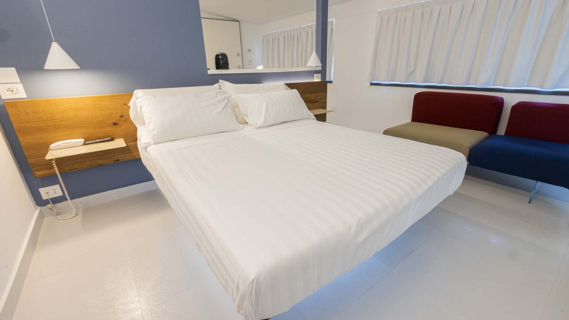 Camera moderna, letto bianco, pareti blu, atmosfera rilassante e accogliente.