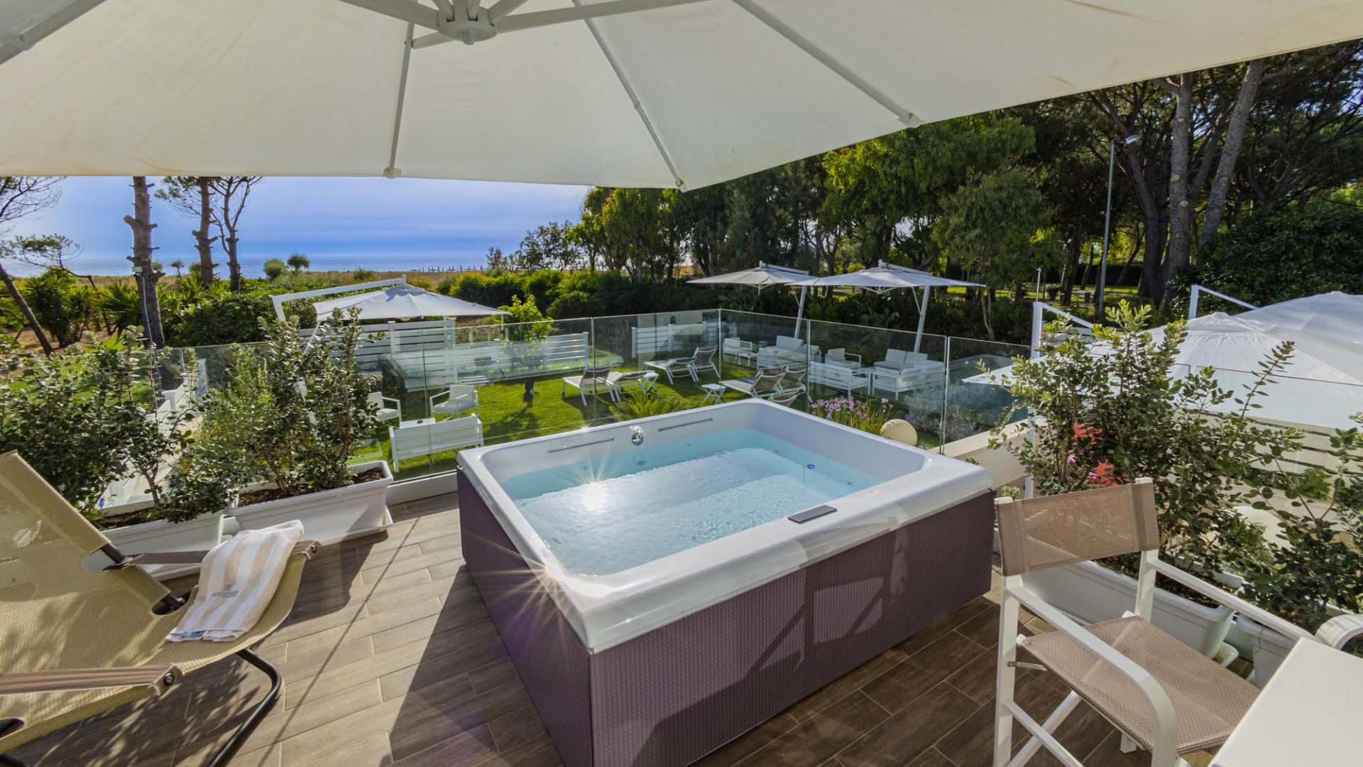Vasca idromassaggio all'aperto con vista mare, circondata da verde e relax.