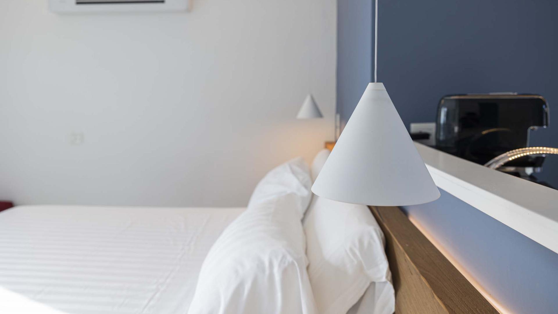 Camera moderna, minimalista, con letto bianco e lampada elegante, atmosfera serena.